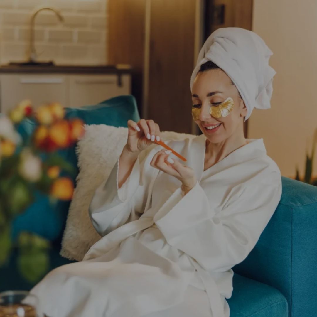 Woman in a white robe with a towel on her head, sitting on a blue couch in a cozy living room.