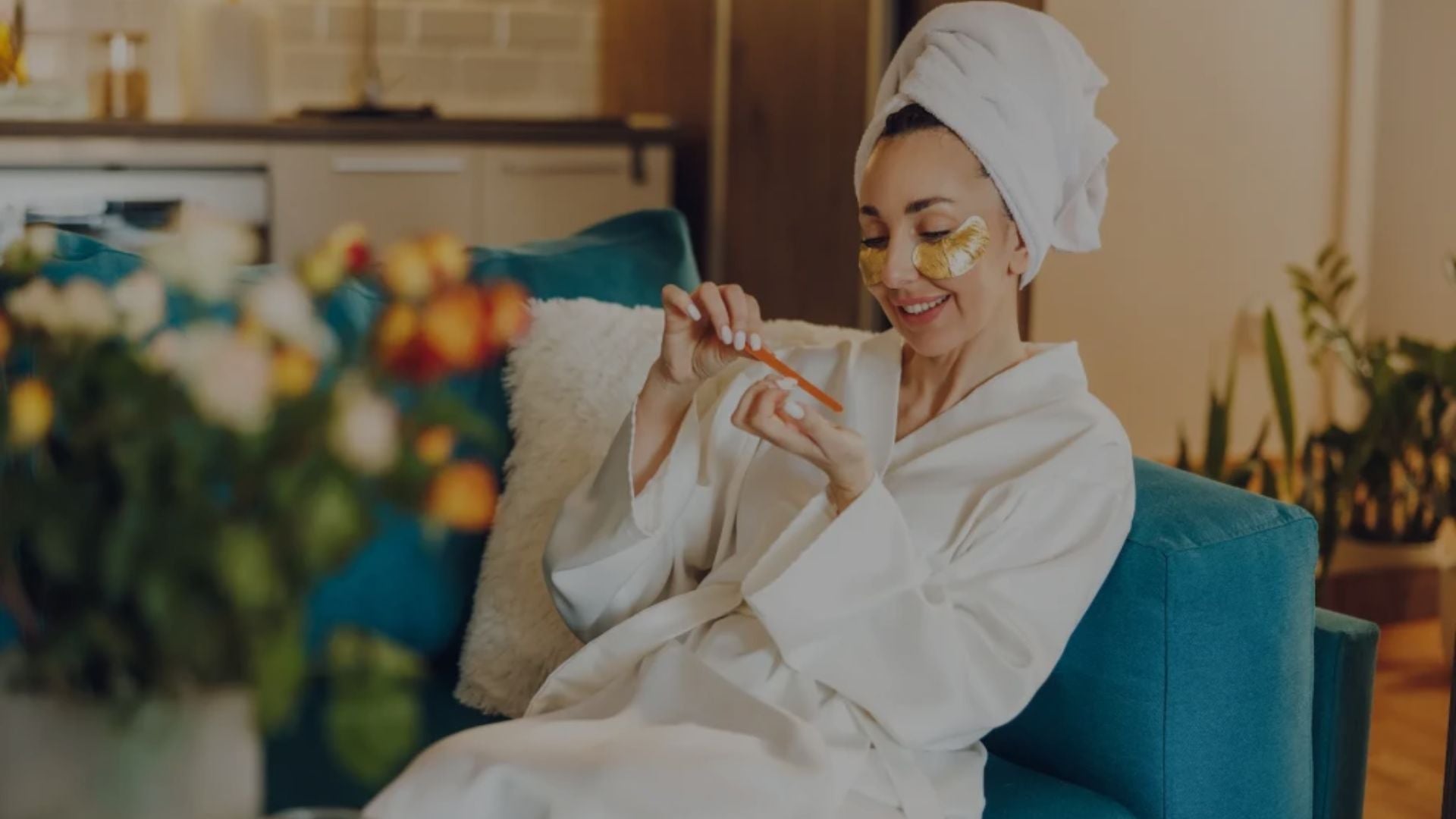 Woman in a white robe with a towel on her head, sitting in a chair, holding a small object.